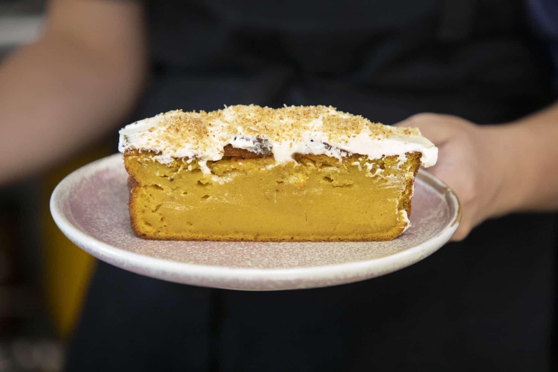 A piece of pumpkin cake with white icing and toasted coconut on top.