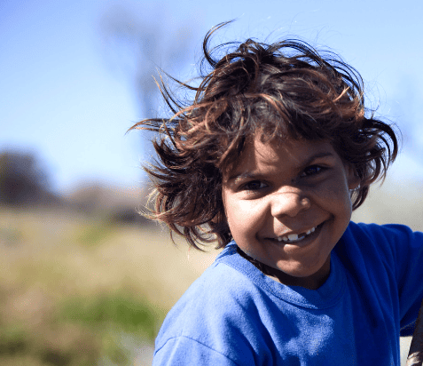 A photo of an Indigenous child. They are wearing a blue shirt and smiling.