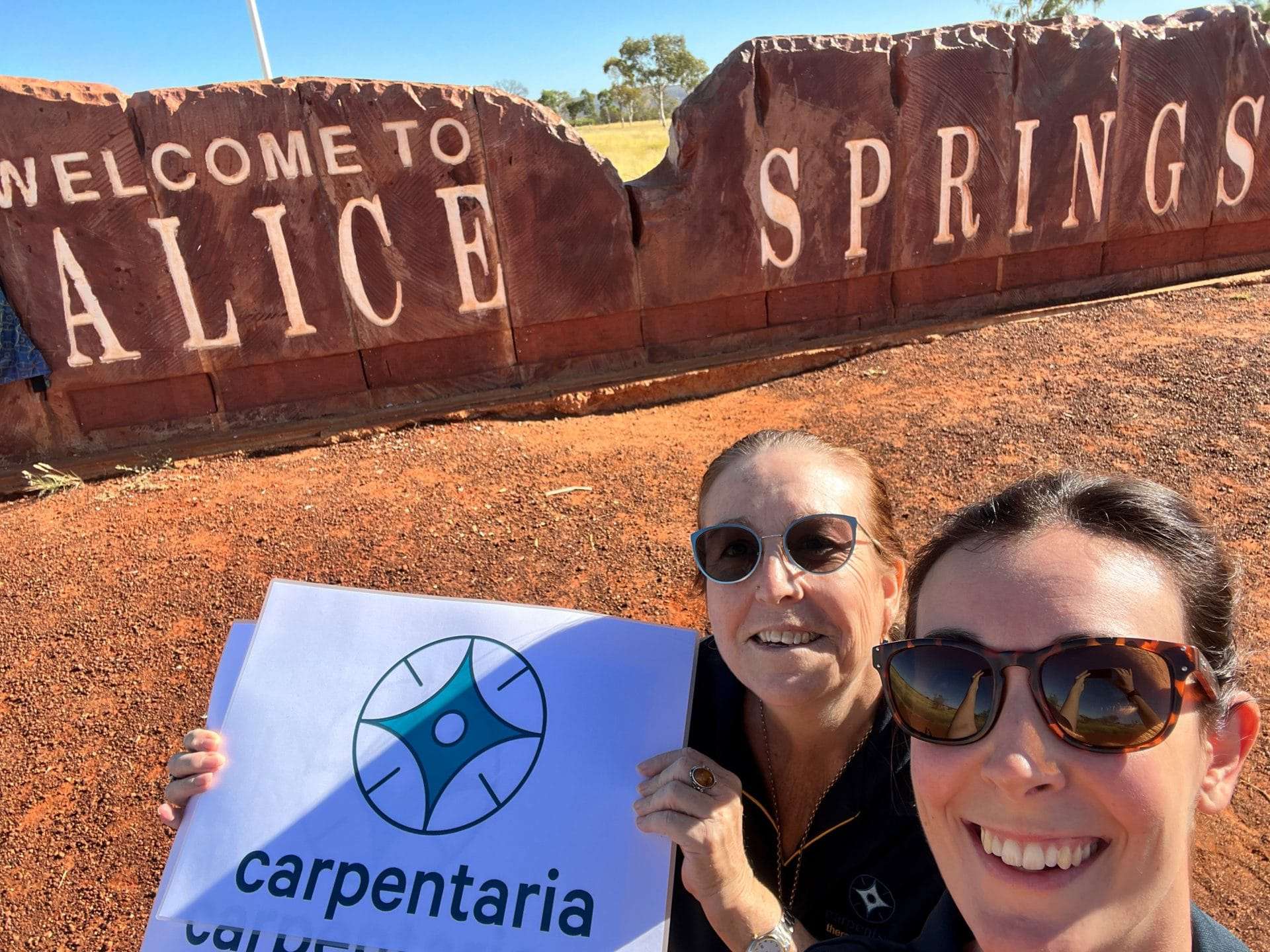 Two Carpentaria staff members in front of a sign which says Welcome to Alice Springs